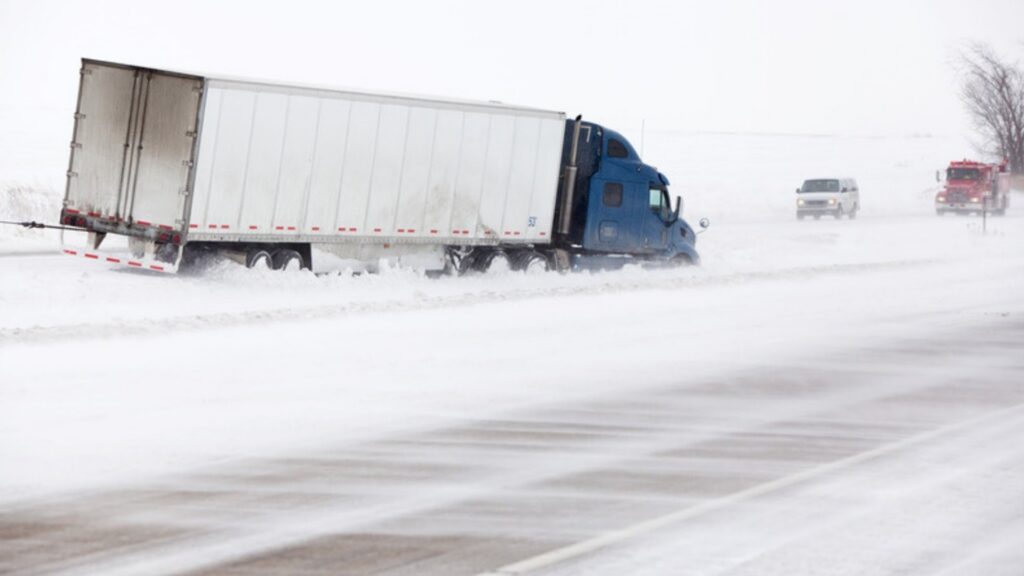 A semi truck slid off a snow-covered highway into the median during blowing snow