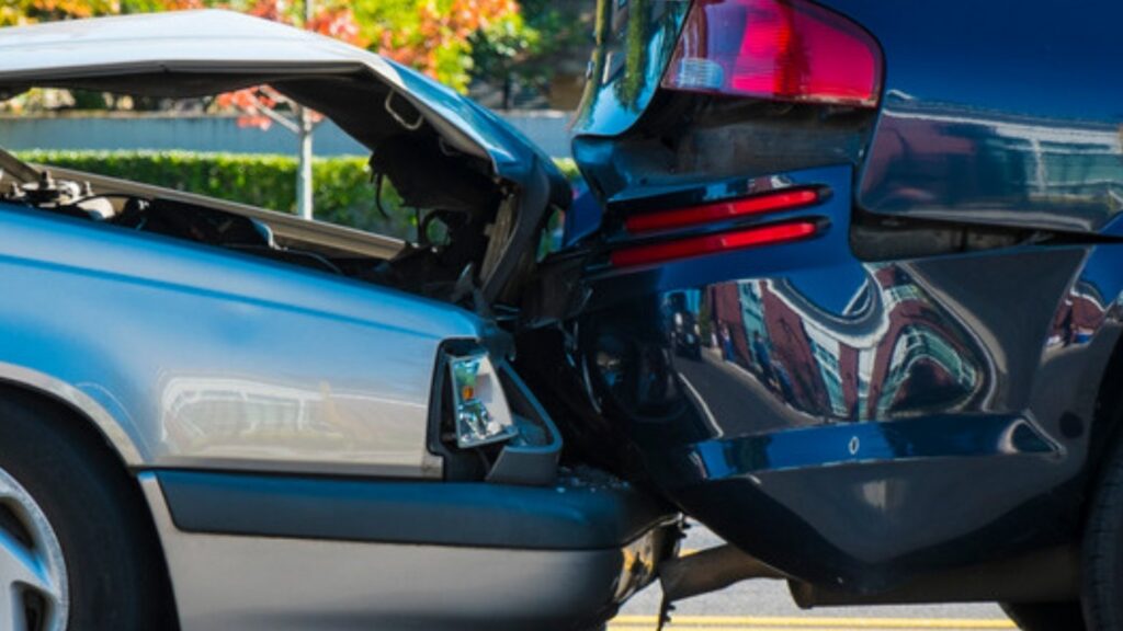 A silver car with a crumpled hood after rear-ending a dark vehicle on a street